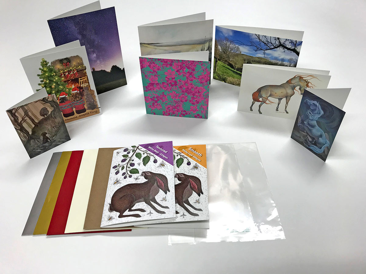 A selection of Redcliffe greeting card products on a white background &mdash; three card finishes (Smooth, Gloss and Textured), illustrated bookmarks, postcards, an assortment of envelope colours, a Certificate of Authenticity and the Redcliffe pen and business card.